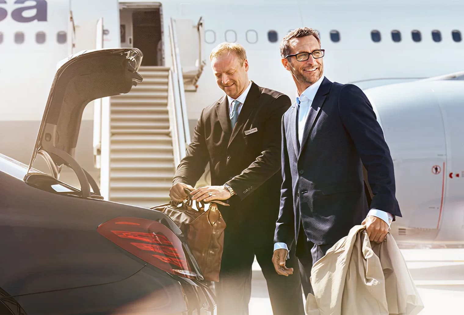 Two men collecting luggage from a car beside an airplane